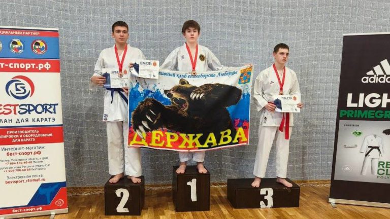 Наш спортсмен на первом месте пьедестала с флагом клуба на Первенстве Тульской области по каратэ