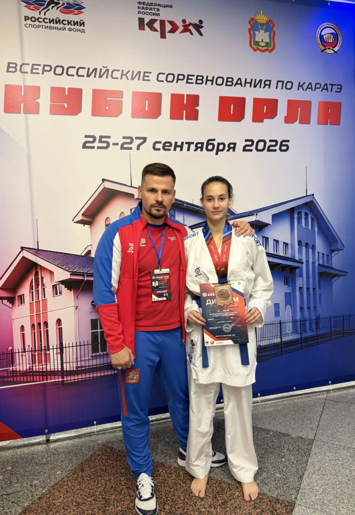 Ворошилова Елизавета с медалью и тренер Воронцов Сергей Сергеевич на фоне баннера соревнований