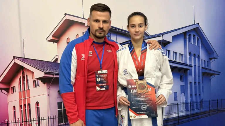 Ворошилова Елизавета с медалью и тренер Воронцов Сергей Сергеевич на фоне баннера соревнований